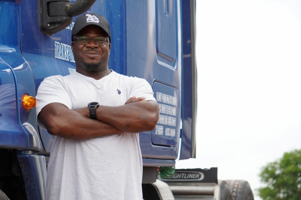 Driver standing next to truck smiling with arms folded